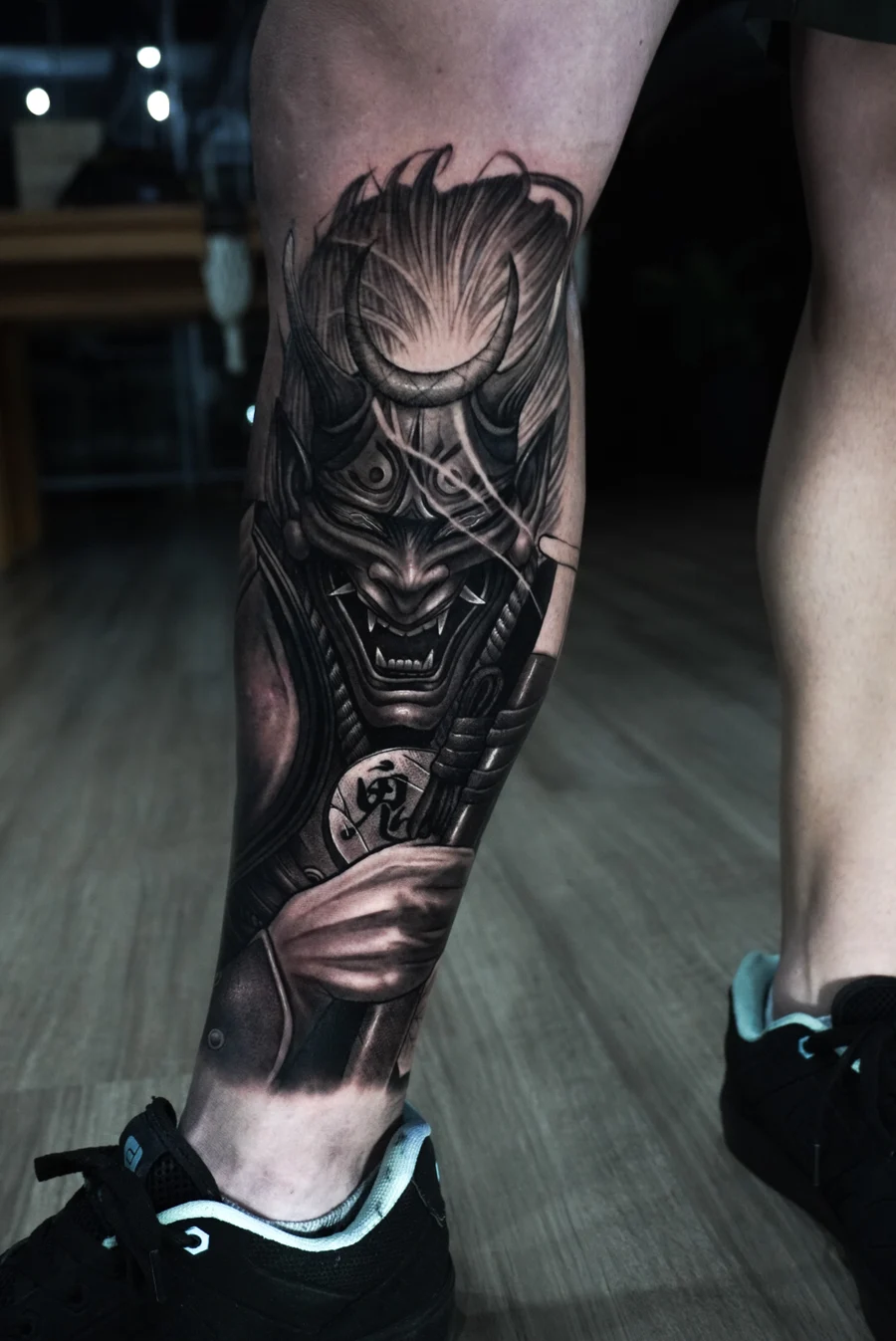 Tatuagem realista de máscara oni samurai em perna, preto e cinza
