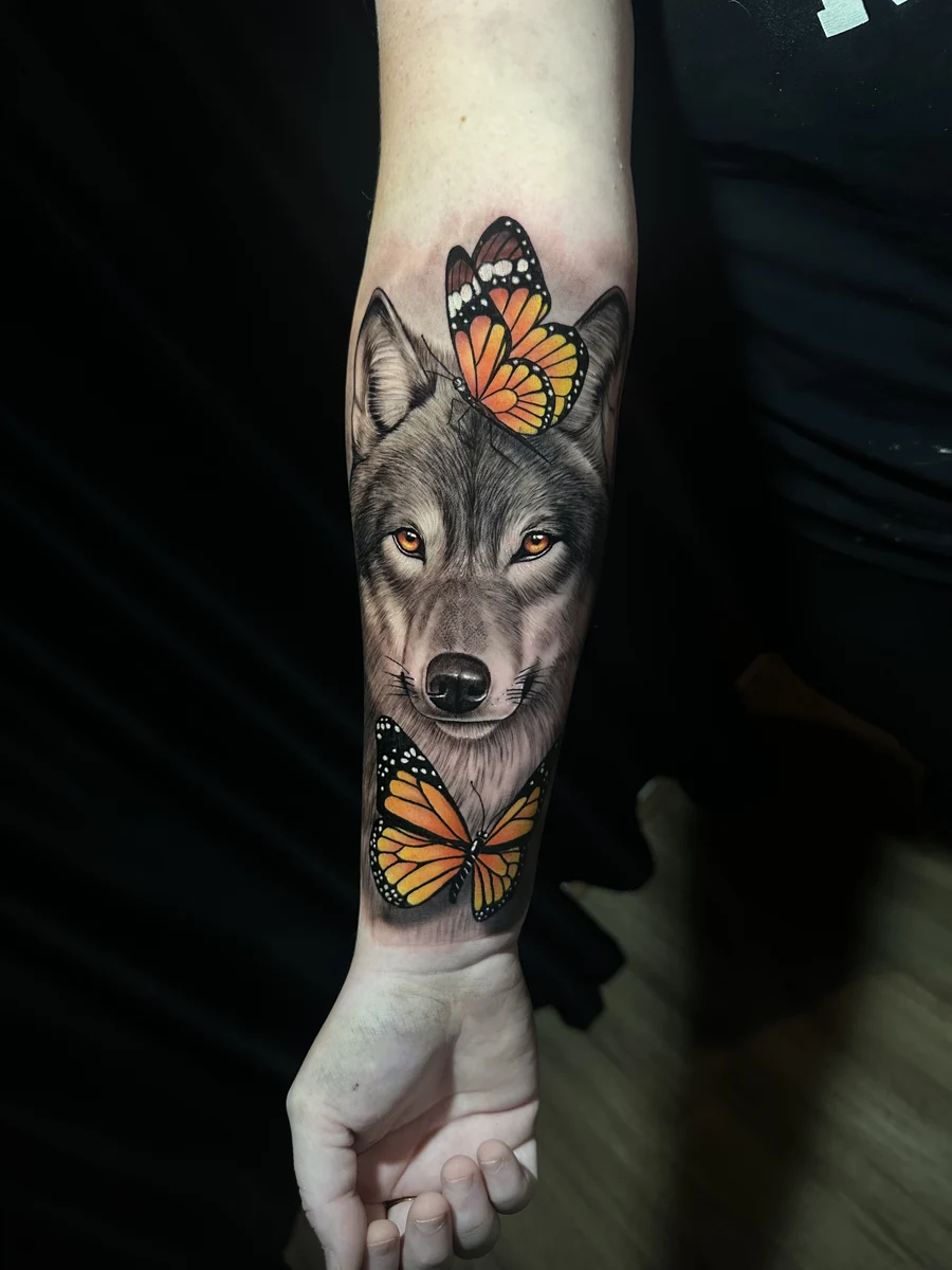 Tatuagem realista colorida de lobo com borboletas monarca, braço